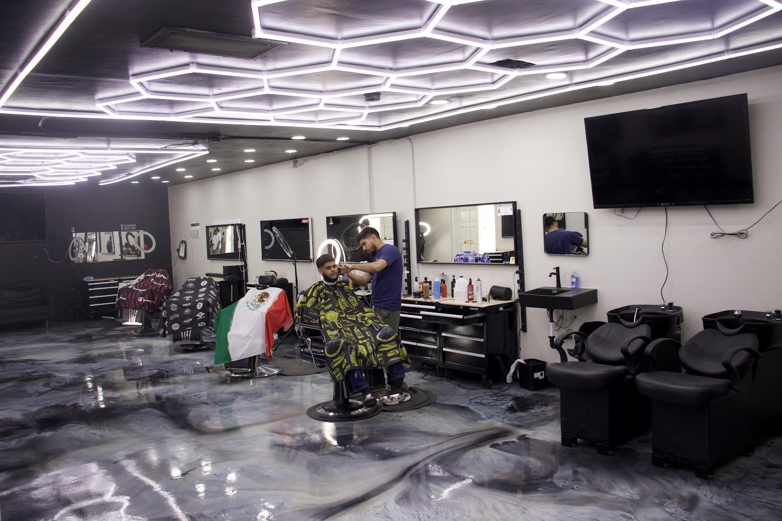Inside Royal Fadez: a barber lines up a client under the glowing hexagon LED ceiling, black chairs and marbled floor around them