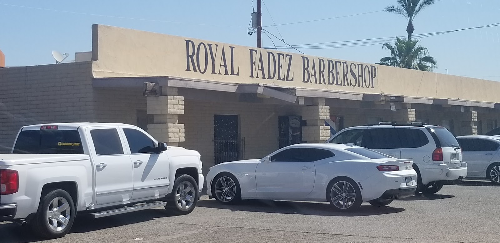 The painted Royal Fadez Barbershop sign over the Arizona Ave storefront, palm tree and desert sky behind