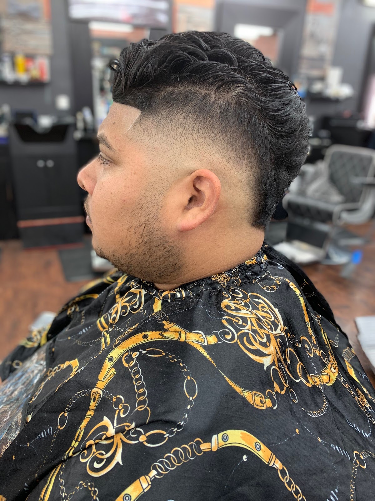 Burst fade with a textured fohawk and razor-sharp front line, client in the gold chain print cape